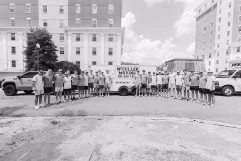 The full McCuller Moving crew in black and white, lined up with the trailer between the residence halls