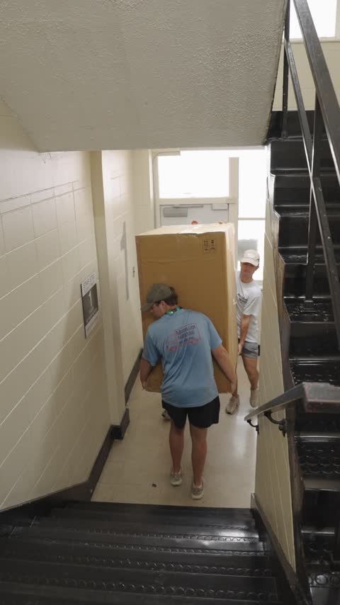 Two crew members easing a large furniture box down a stairwell landing