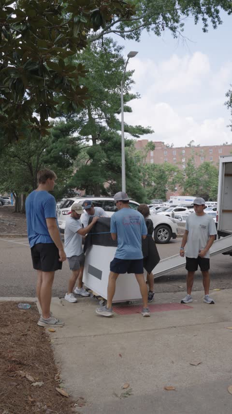 The crew strapping a blanket-wrapped dresser to a cart at the tail of the trailer