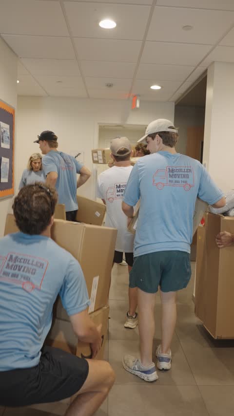 The crew hand-carrying boxes single file through an apartment hallway