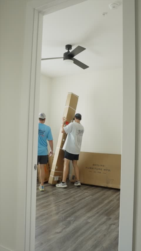 Two crew members standing a tall flat-pack furniture box upright in an empty apartment bedroom