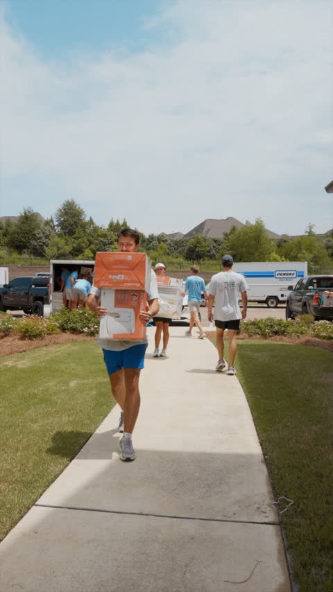 Crew members carrying boxed furniture up a front walk with the trucks staged at the curb