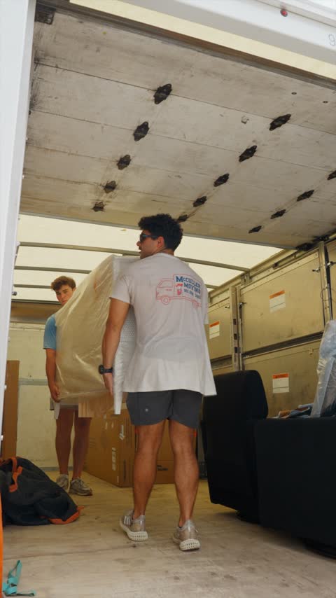 A crew member shouldering a plastic-wrapped mattress inside the truck