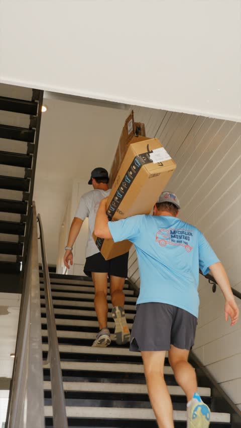 Two crew members carrying long boxed furniture up an apartment staircase