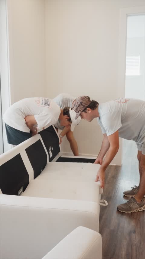 Crew members setting a new white couch in place in an apartment living room