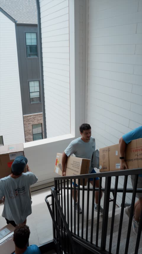 Crew members carrying shipped boxes up an apartment stairwell