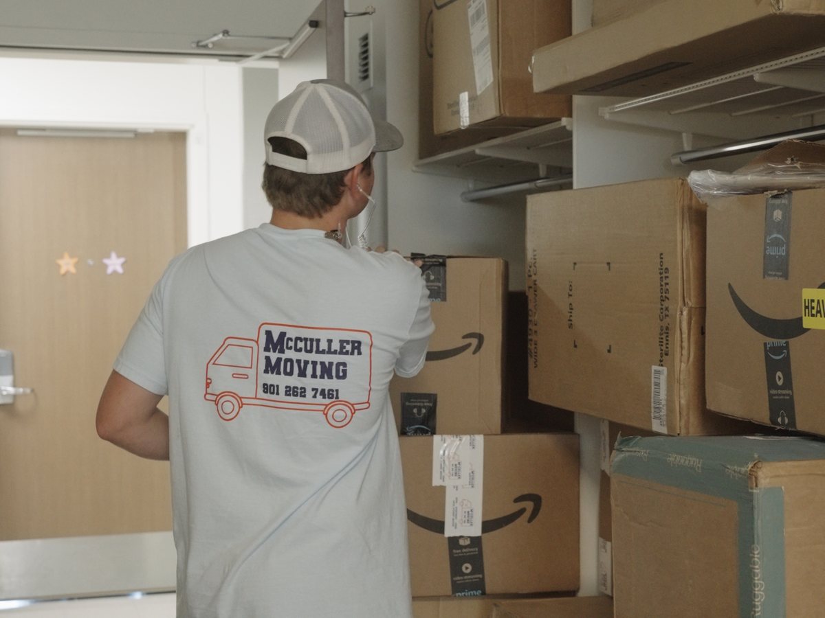 A McCuller Moving crew member beside a wall of shipped Amazon and Sterilite boxes waiting for move-in